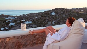 A person relaxing on a balcony with a view of a coastal landscape, including white buildings and rocky terrain. - Sea & Stone Residence Mykonos (Mykonos)