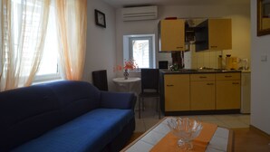 A compact living space with a sofa, a dining table, a kitchen area, and a window with curtains. - Zdenac Studio (Rovinj)