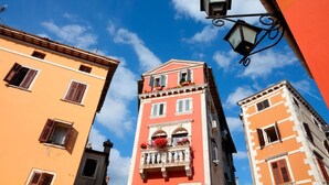 A tall building with a pink facade and a balcony with red flowers. - Zdenac Studio (Rovinj)