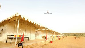 Un campamento en el desierto con tiendas, camas numeradas y un paisaje arenoso.