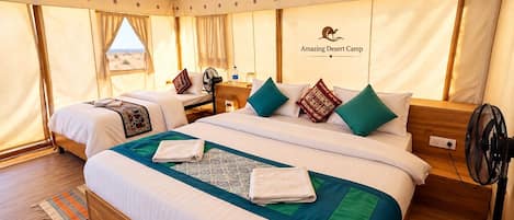 A tented accommodation with two beds, a fan, and a view of the desert.