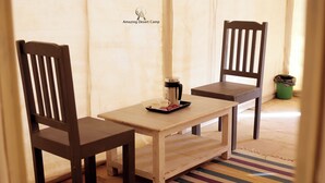 Una mesa de madera con dos sillas, una bandeja con una taza y un termo, y una alfombra a rayas.