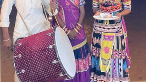 A group of people in traditional attire, one playing a drum, standing in an outdoor setting with tents in the background. - Amazing Desert Camp (Jaisalmer)