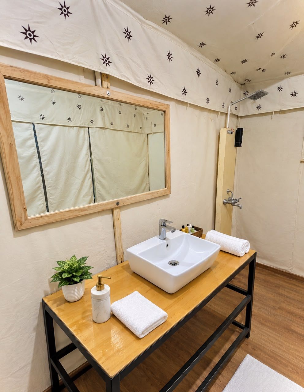A bathroom with a wooden vanity, a white sink, a mirror, a towel, a plant, and a shower area.