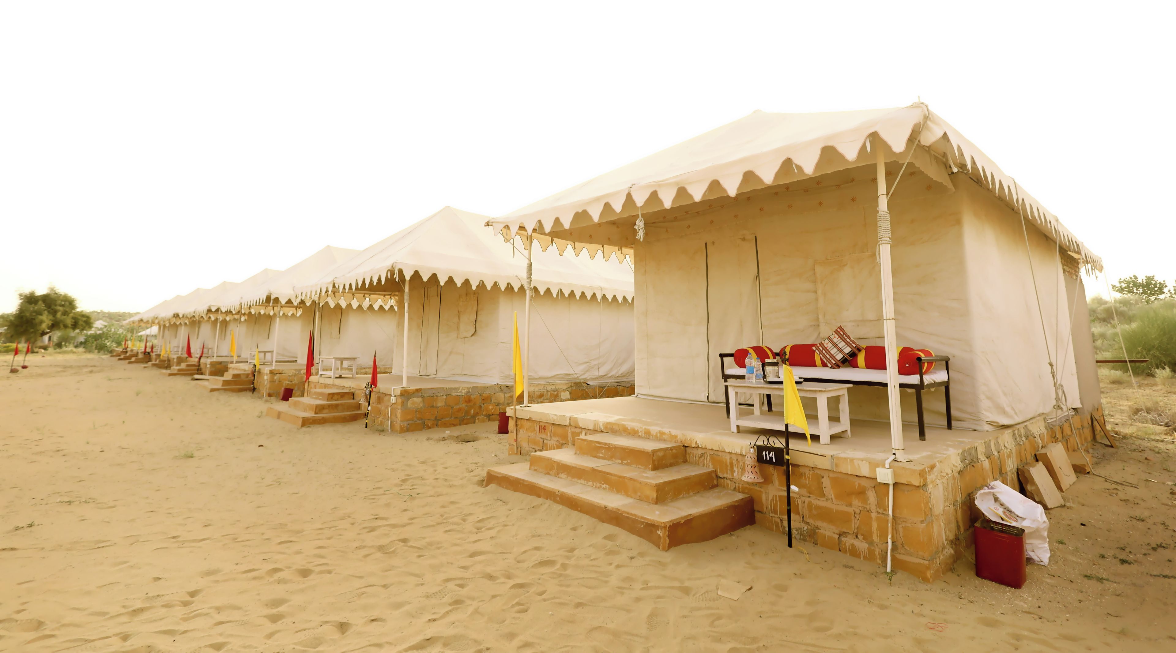 Fileira de tendas no deserto, com escadas que levam à entrada, cada uma com uma pequena mesa e almofadas.