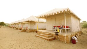 A row of desert tents with steps leading up to the entrance, each with a small table and cushions. - Amazing Desert Camp (Jaisalmer)