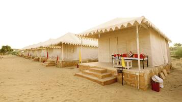 Fileira de tendas no deserto, com escadas que levam à entrada, cada uma com uma pequena mesa e almofadas.