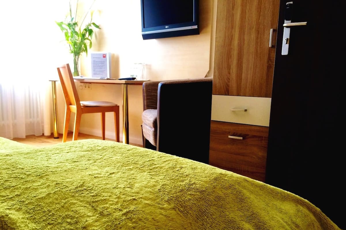 A hotel room with a bed, a desk, a chair, a TV, and a wardrobe.