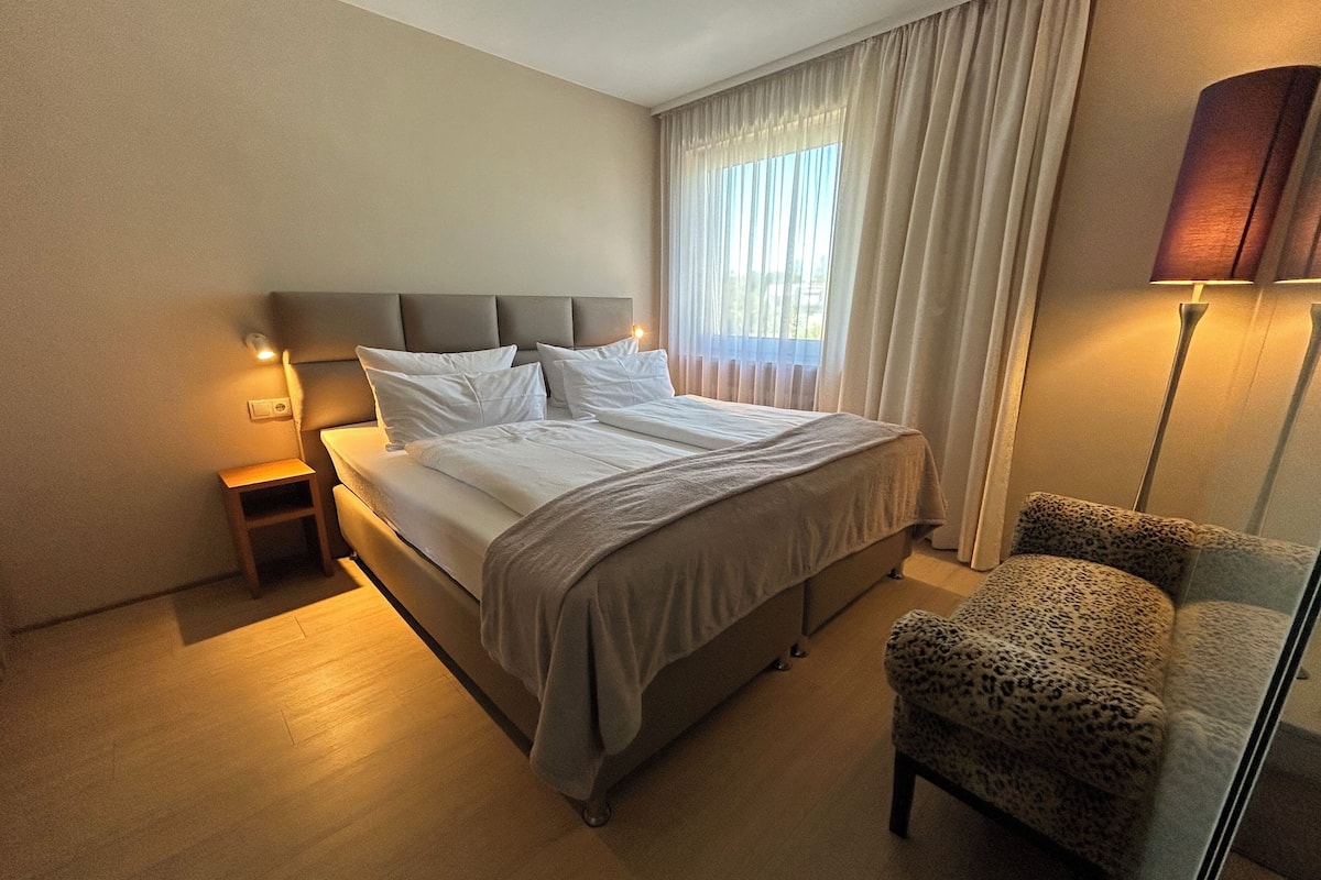 A hotel room with a bed, a nightstand, a chair, and a lamp.