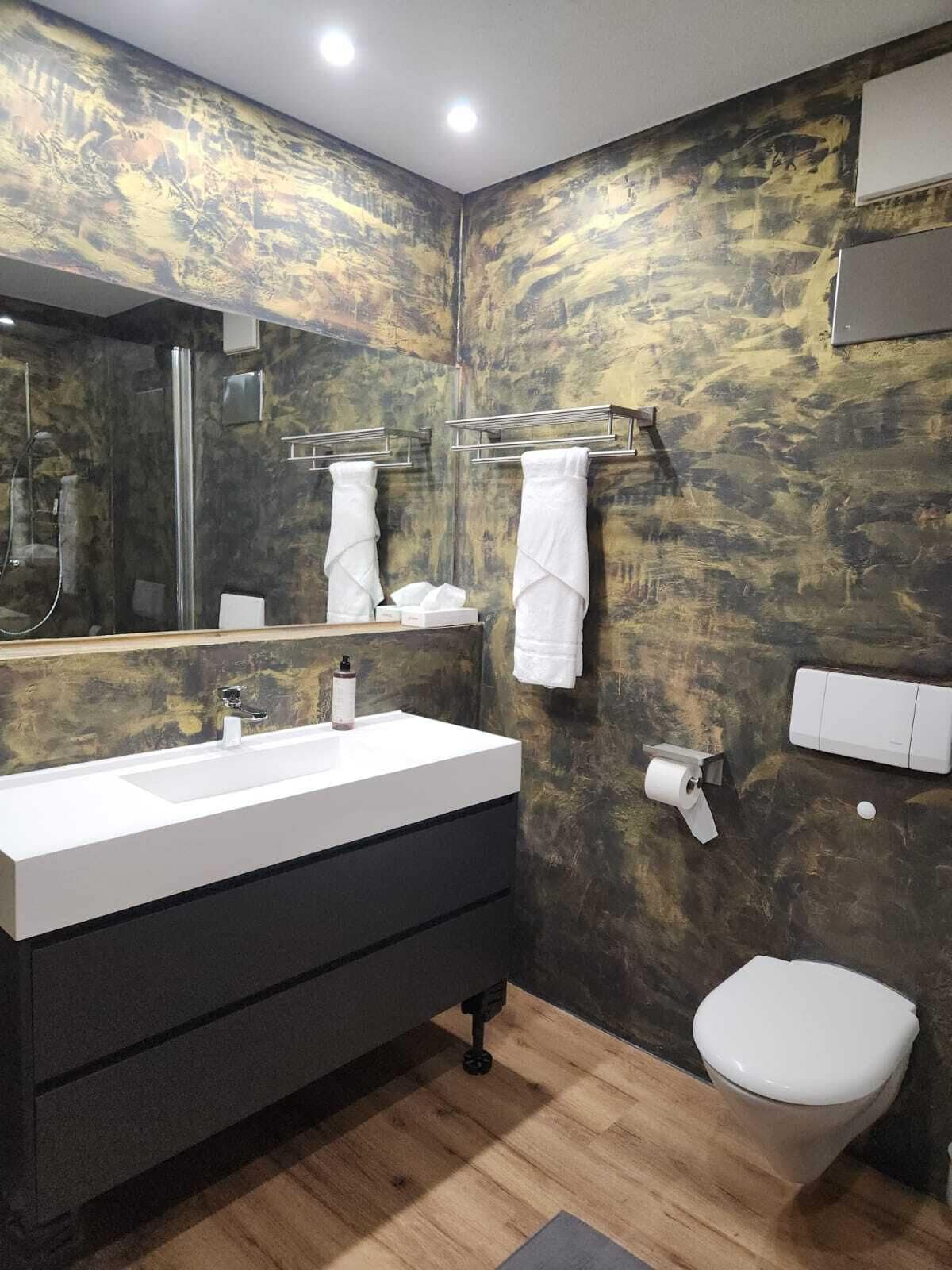 A modern bathroom with a large mirror, a white sink, a toilet, and a towel rack.