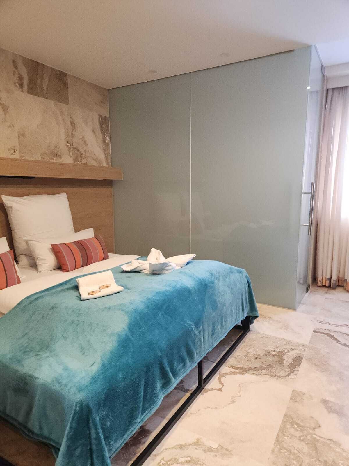 Ein Hotelzimmer mit einem Bett, einem Kopfteil, einem großen Fenster mit Vorhängen und einem Marmorboden.