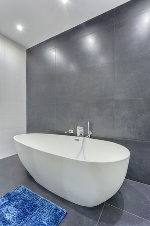 Ein modernes Badezimmer mit einer freistehenden Badewanne, dunklen Fliesenwänden und einem blauen Teppich.