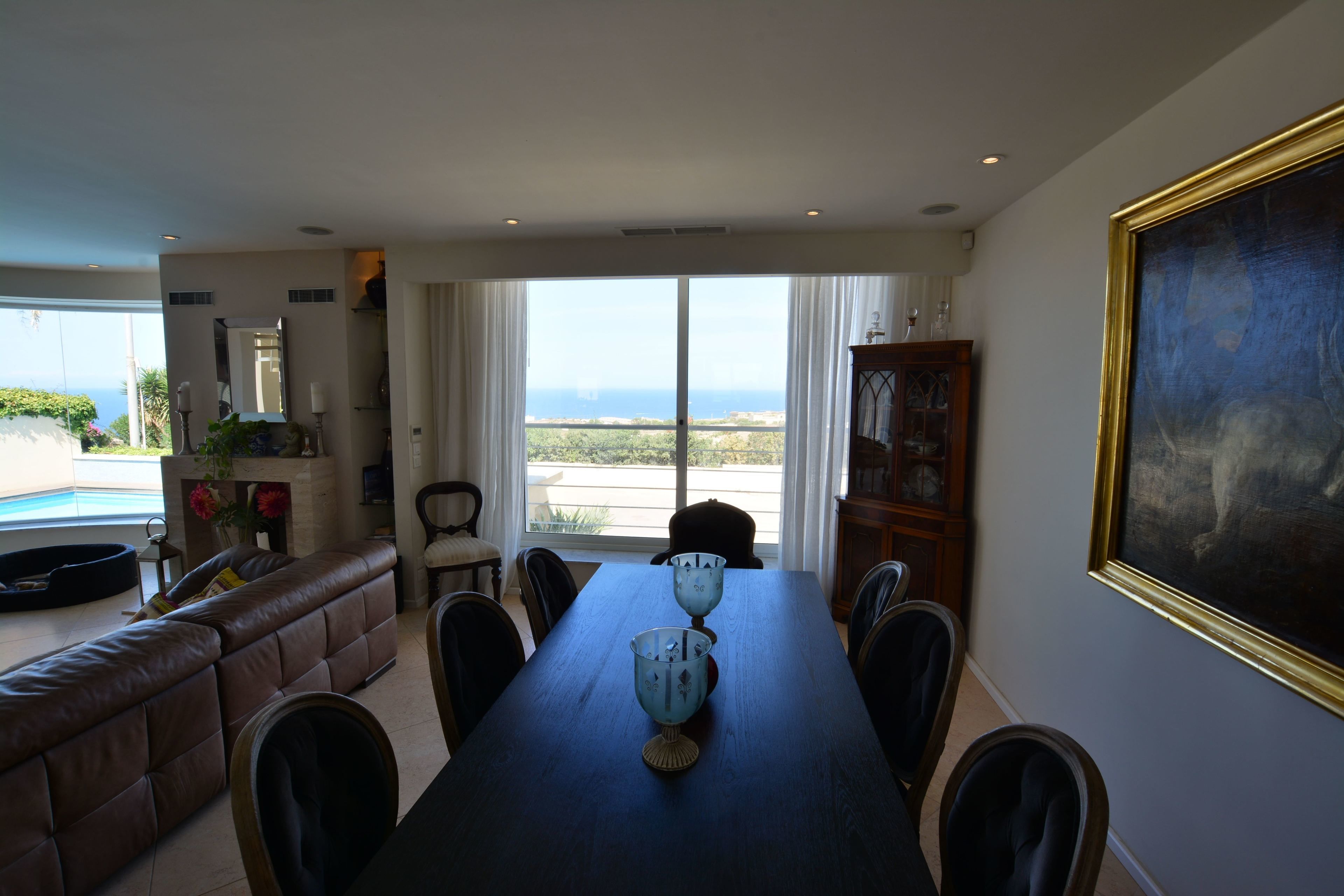 A dining area with a long table, chairs, and a view of the ocean through large windows.