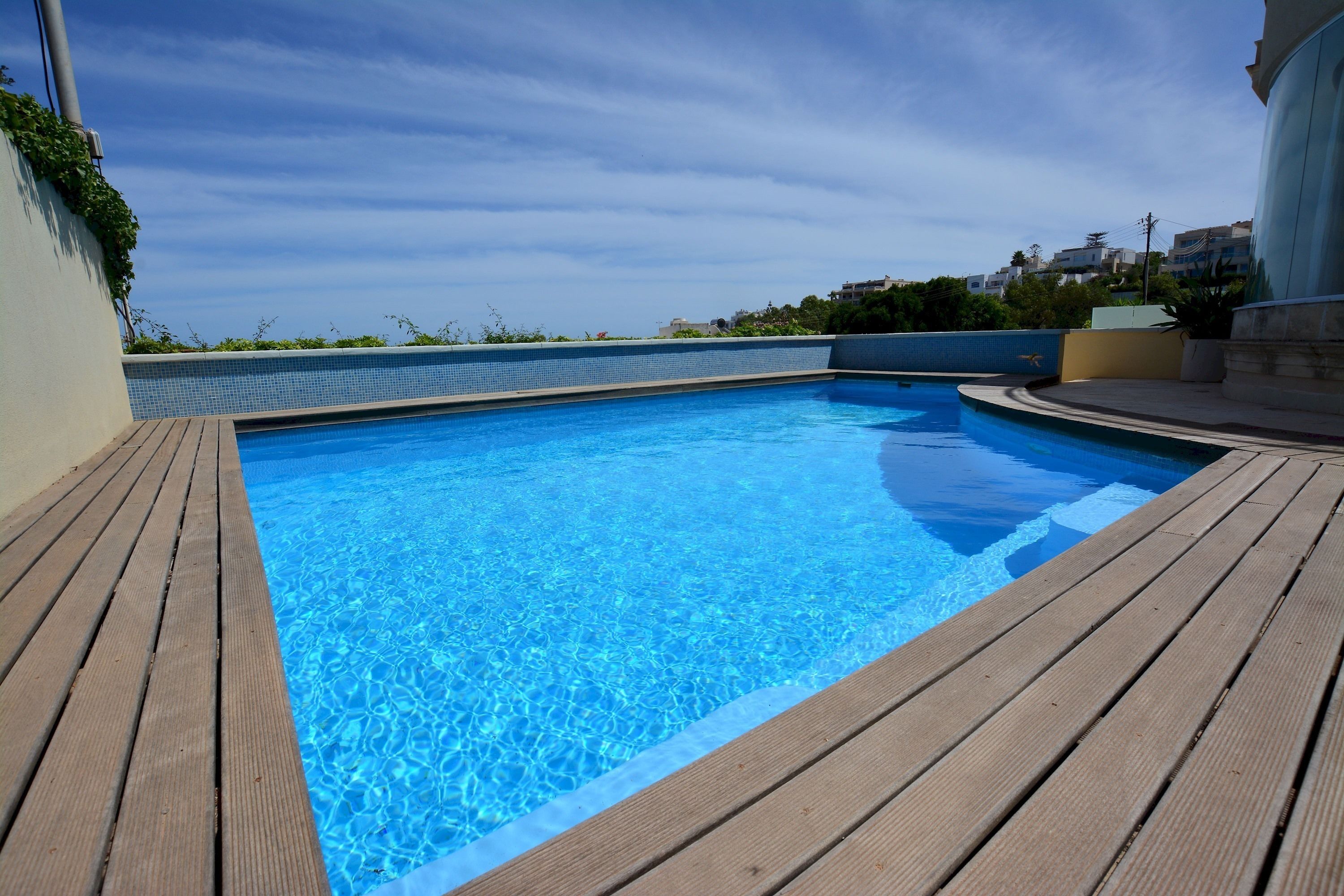 A rectangular swimming pool with clear blue water, surrounded by a wooden deck.