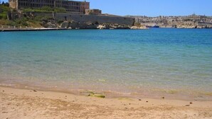 A coastal scene with a large building on a cliff overlooking the sea. - Charming Seafront House In Kalkara (Kalkara)