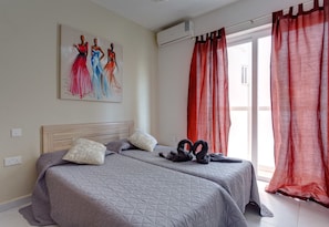 A bedroom with two beds, a painting on the wall, and red curtains.
