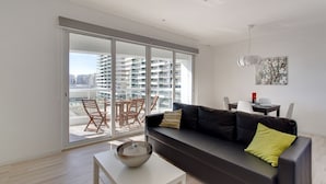 Uma sala de estar moderna com um sofá preto, uma mesa de centro branca e uma área de jantar com mesa e cadeiras.
