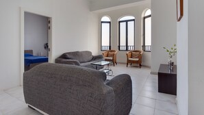Un salon avec un canapé gris, une petite table, des chaises en osier et une vue à travers des fenêtres en arc de cercle.