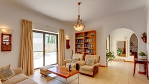 Een ruime woonkamer met een grote boekenkast, comfortabele zitplaatsen en uitzicht door een schuifdeur op een buitenruimte.