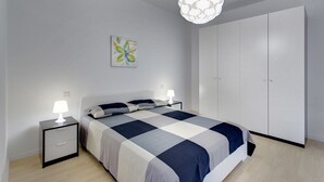 A bedroom with a bed, two bedside tables with lamps, a wardrobe, and a wall-mounted light fixture. - Modern Apartment With Stunning Seaviews (Sliema)