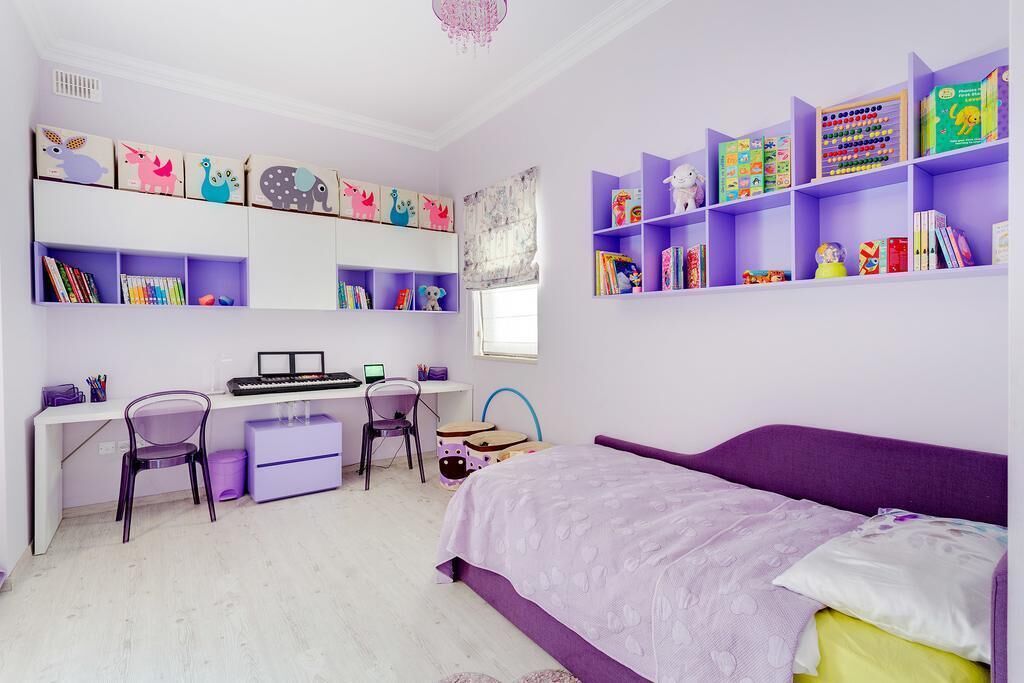 A child's bedroom with a purple bed, a desk with a computer, and shelves with books and toys.