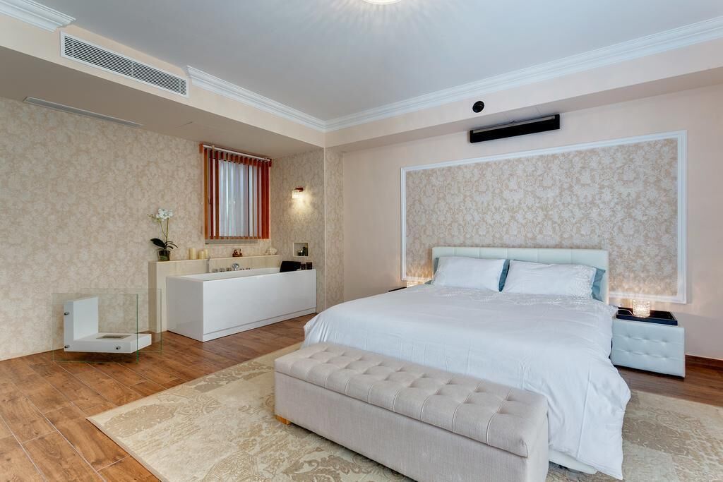Un dormitorio moderno con una cama grande, un banco empotrado, un tocador con espejo y una bañera.