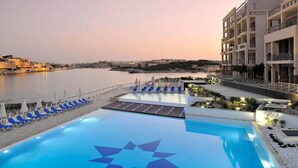 Une piscine en forme d’étoile, des chaises longues et une vue sur la mer et les bâtiments.
