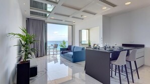 A modern kitchen with a central island, a dining area with bar stools, and a large window overlooking the sea.