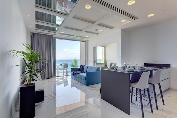 A modern kitchen with a central island, a dining area with bar stools, and a large window overlooking the sea.
