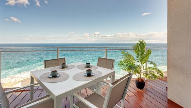 A table with four cups and saucers on a deck overlooking the ocean.