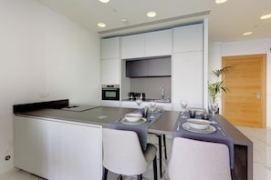 A modern kitchen with a central island, built-in appliances, and a dining area with two chairs and a table set for two.