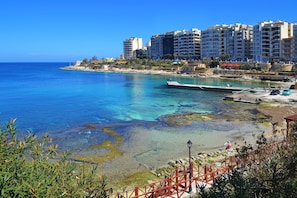 A coastal cityscape with clear blue waters, a pier, and high-rise buildings.