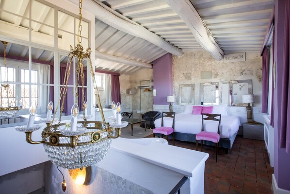 A hotel room with a chandelier, a bed, a desk, and a window with curtains.