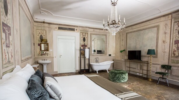 A spacious bedroom with a large bed, a clawfoot bathtub, a television, and a chandelier. - Oltrarno Splendid (Florence)