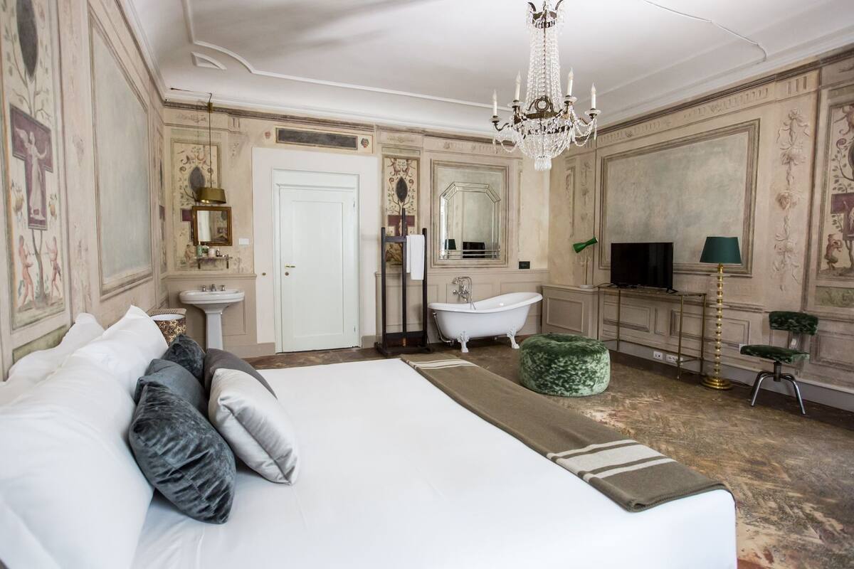 Um quarto espaçoso com uma cama grande, uma banheira de pés de leão, uma televisão e um candelabro.
