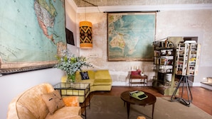 A living room with a large map, a yellow sofa, a coffee table, and a bookshelf filled with books and decorative items. - Oltrarno Splendid (Florence)
