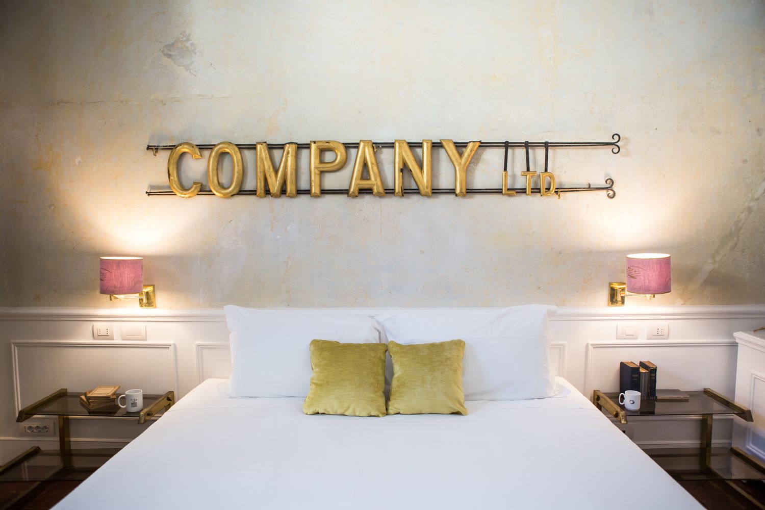 A hotel room with a large bed, two bedside tables, a nightstand, and a wall-mounted sign that reads "COMPANY LTN".