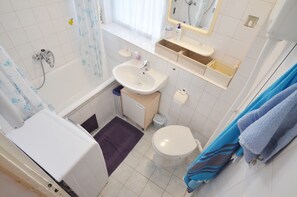 Un baño pequeño con bañera, lavamanos, inodoro y un espejo sobre el lavamanos.