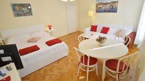 Een hotelkamer met een bed, een bank, een eettafel en stoelen. Er hangt een schilderij aan de muur en op het nachtkastje staat een lamp.