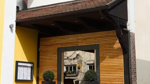 Ingresso di un edificio con facciata in legno, stipite della porta nero e due piante in vaso.