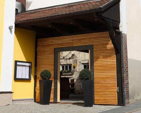 Entrada de un edificio con fachada de madera, marco de puerta negro y dos macetas.