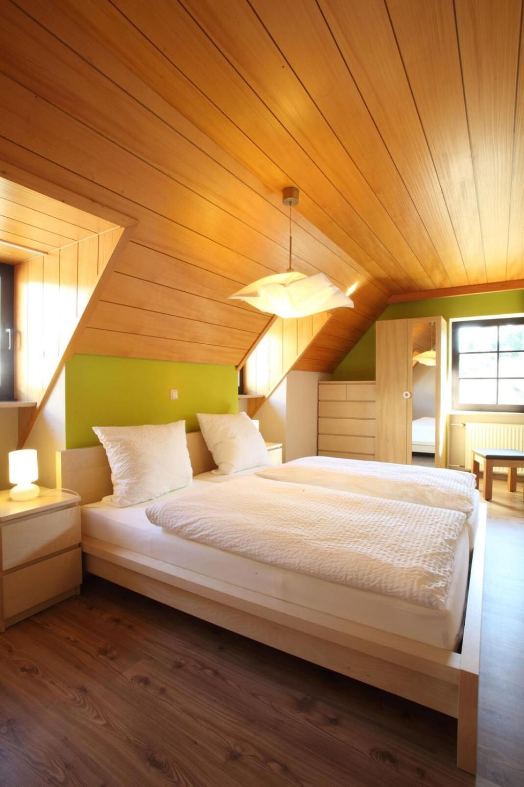 A bedroom with a sloped ceiling, a bed, a nightstand, a lamp, and a window.