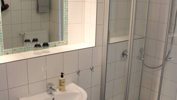 Un baño con lavamanos blanco, un espejo, cabina de ducha y un taburete pequeño.