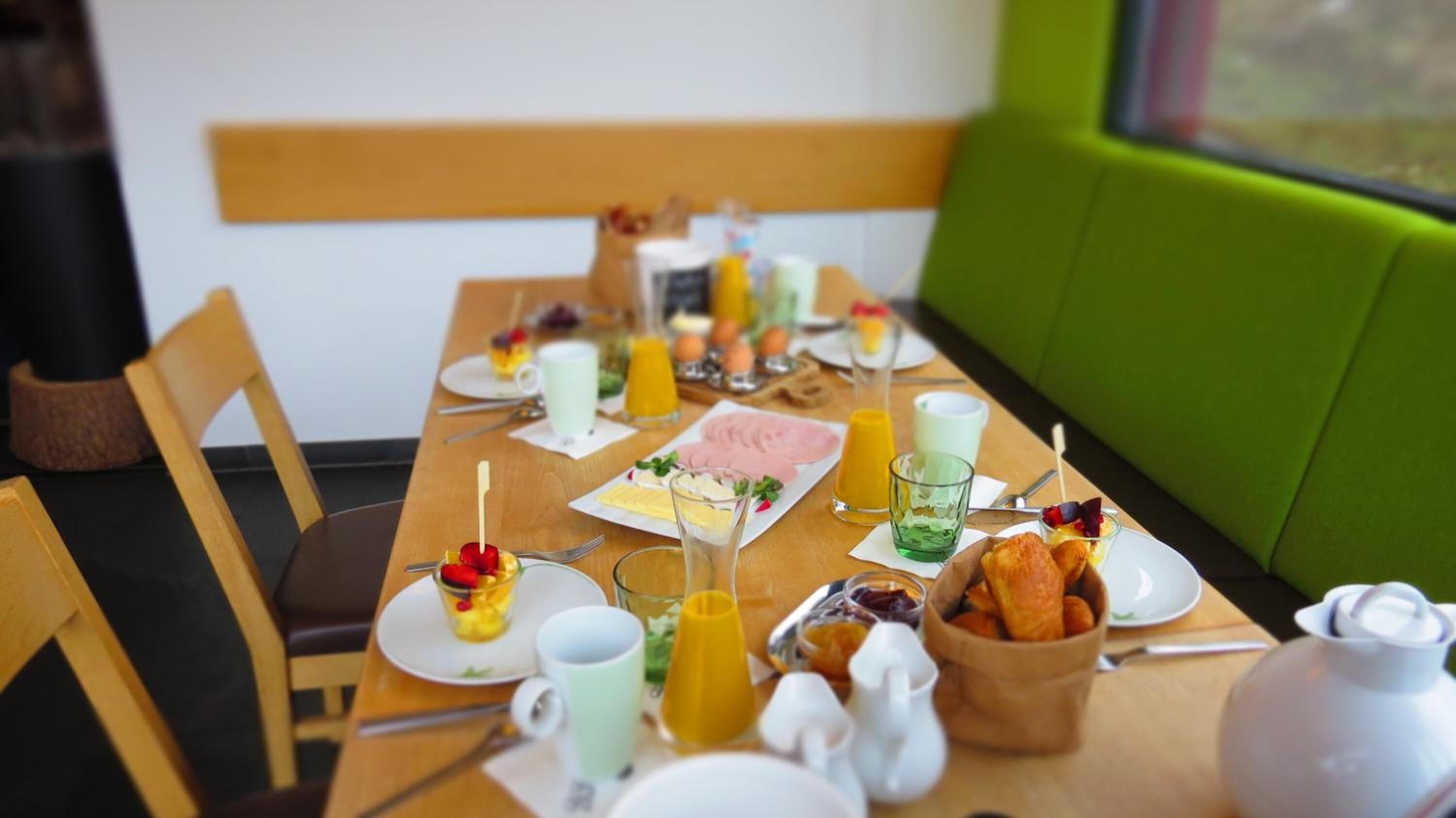 Une table de petit-déjeuner dressée avec des assiettes, des verres et un saladier rempli de viennoiseries.