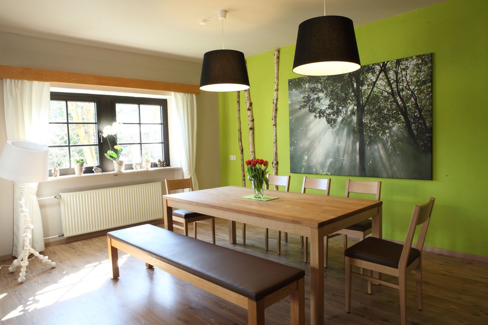 Een eetgedeelte met een houten tafel, stoelen, een bank en een groot raam met gordijnen.