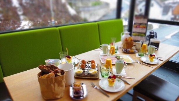 Una tavola imbandita per la colazione, con diversi piatti, bevande e posate, e vista all'esterno attraverso una finestra.