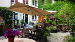 Zona patio esterna con tavoli e panche in legno, circondata da vasi con piante e fiori.