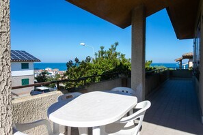 A balcony with a table and chairs, a view of the sea, and buildings in the background. - M117 - Marcelli, four-room apartment with sea view terrace (Marcelli)