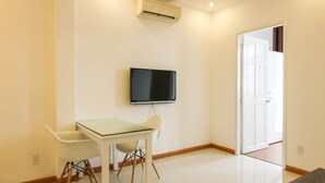 A room with a glass table and chairs, a mounted TV, and a white door.