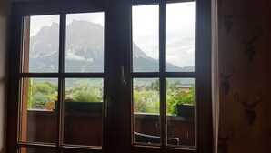 Une pièce dotée d’une grande fenêtre donnant sur un paysage montagneux et un village situé en contrebas.